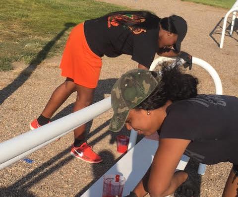 Members of the women's basketball team (Kiyah Clark and Monique Schuman) painting a bench for "Paint The Parks"
